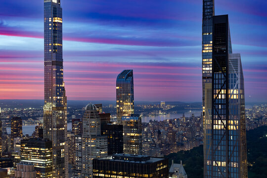 Aerial view of Midtown Manhattan at dusk showing tall residential skyscrapers of Billionaires Row, the upper West Side, Hudson River, and the edge of Central Park under a colorful sunset sky.