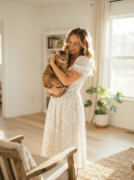 Woman in a floral dress holding a large orange cat indoors under gentle light
