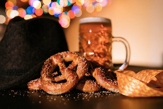 Pretzels with a beer stein and traditional alpine hat on a dark surface, featuring salted crust and golden foam for Bavarian festival and hospitality