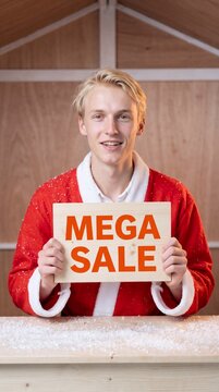 Young man in Santa costume holds a mega sale sign