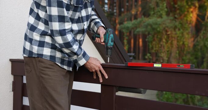 Worker installing wooden balcony railing with screwdriver during house construction