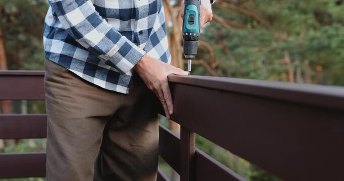 Worker installing wooden patio railing with screwdriver during house construction