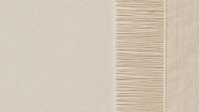 A close-up image of beige woven fabric with a fringe of evenly spaced threads on one side.