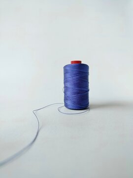 blue sewing thread spool on white background with loose thread