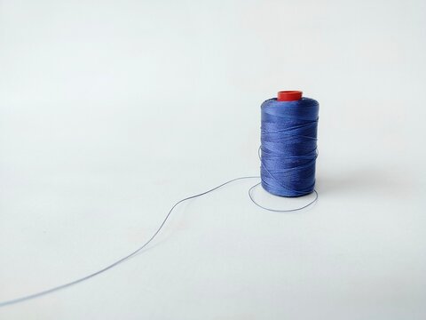 blue sewing thread spool on white background with loose thread