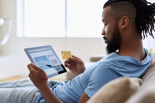 Close-up shot of a Black man holding a digital tablet and shopping online on Black Friday at home. African American Man shopping online with credit card and digital tablet.