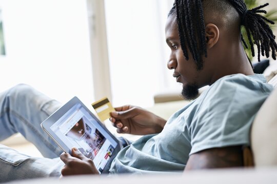 Close-up shot of a Black man holding a digital tablet and shopping online on Black Friday at home. African American Man shopping online with credit card and digital tablet.