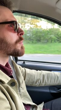 A bearded man wearing sunglasses is driving, view from inside the car, slow-motion footage