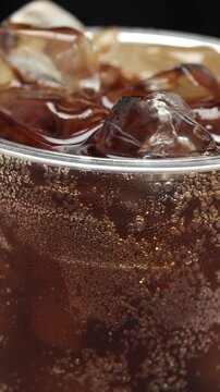 Slow motion soft drink vertical pouring with ice cubes and bubbles, 