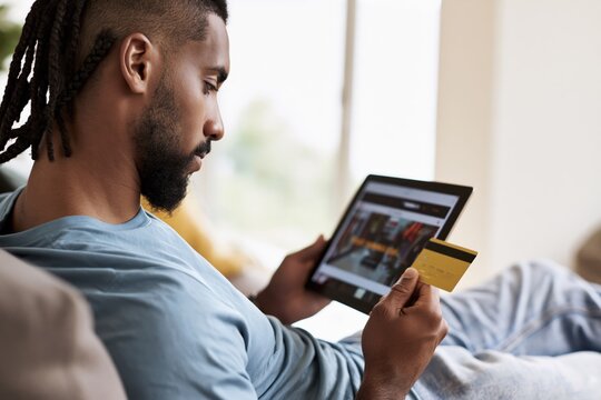 Close-up shot of a Black man holding a digital tablet and shopping online on Black Friday at home. African American Man shopping online with credit card and digital tablet.