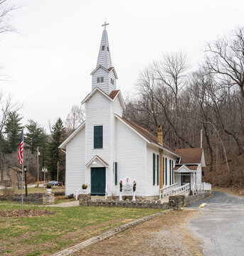 Grafton, Illinois, United States - 04 August 2026: View of a historic white wooden church with a steeple and green doors, set against a backdrop of leafless trees in a rural landscape.