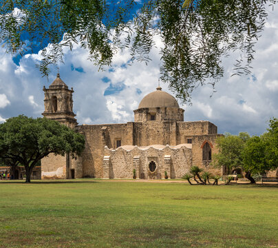 San Antonio, United States - 05 August 2026: View of Mission San Jose with historic stone architecture, bell tower, and dome under a blue sky with white clouds in a park.