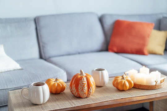 Autumn fall mood composition for hygge home decor. Hot tea or coffee drink in pumpkin's shaped cups, pumpkin decor and burning candles on the coffee table. Festive autumn, fall mood home decor
