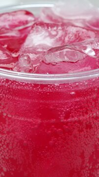 Slow motion soft drink red vertical pouring with ice cubes and bubbles, 