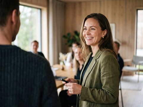 Smiling female manager greeting team during workplace meeting in warm modern office with confident professional expression and collaborative atmosphere