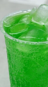 Slow motion soft drink green vertical pouring with ice cubes and bubbles, 