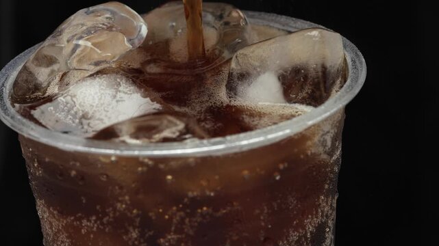 Slow motion soft drink pouring with ice cubes and bubbles.