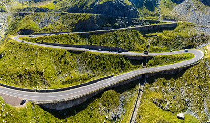Obraz premium Curving Alpine Road Cutting Through Green Carpathian Mountains. Mountain Infrastructure and Serpentine Highway. A road with successive serpentines