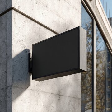 Blank black rectangular sign on a concrete building wall, urban setting.