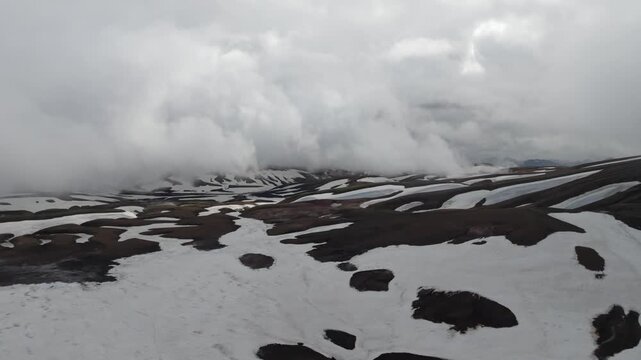 Aerial drone pan left of the Laugavegur hiking trail on Iceland. Discover a remote, rugged volcanic snowscape with patchy snow and mountains under an overcast sky, inspiring solitude and adventure.