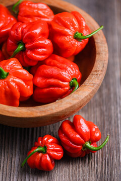 Close view of red habanero peppers in wooden bowl with few outside. Fresh chili pods natural texture rustic background