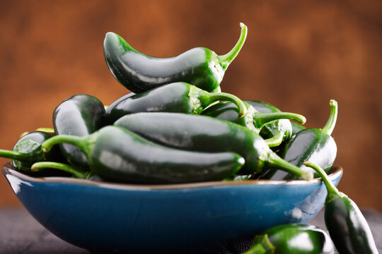 Bowl of jalapeno peppers on wooden table with warm tones and soft focus background. Fresh chili, organic produce, still life composition
