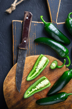 Black jalapeno with knife on rustic wooden cutting board close up. Green mexican jalapeno hot peppers