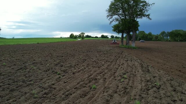 Freshly plowed cloddy soil with tractor and trees under stormy sky