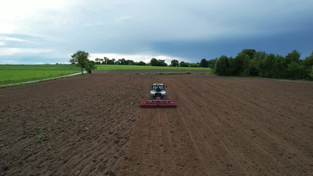 White tractor with red harrow facing camera on freshly worked field