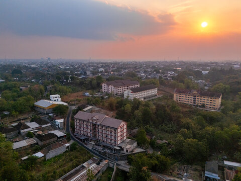 Aerial view of the cityscape of Surakarta at sunset, featuring residential buildings, lush greenery, and urban infrastructure in Surakarta, Central Java, Indonesia.