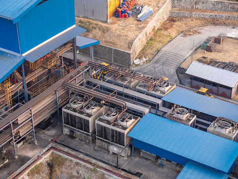 Aerial view of an industrial facility featuring large cooling towers, complex metal piping systems, and blue metal roofing in an industrial zone in Surakarta, Central Java, Indonesia.