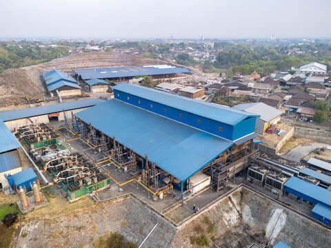 Aerial view of a waste to energy power plant with blue roofs and industrial machinery situated near residential buildings in Surakarta, Central Java, Indonesia.