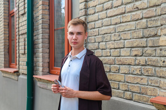 Young blonde man in brown clothing standing on a European city street with classic architecture and urban lifestyle atmosphere.