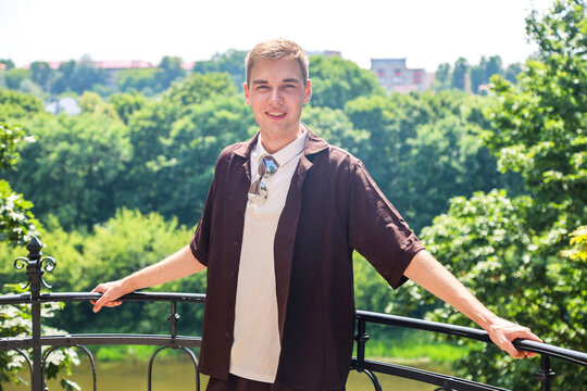 Young man standing on a high mountain top enjoying the panoramic view of the city below on a sunny summer day, travel and adventure concept.