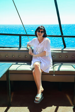 Brunette woman sunglasses standing on the open deck of a cruise ship enjoying ocean views and relaxing vacation travel lifestyle.