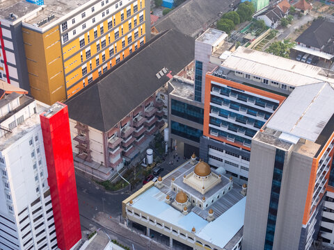 Aerial view of a mosque with golden domes situated between modern high-rise buildings and urban streets in Surakarta, Central Java, Indonesia.