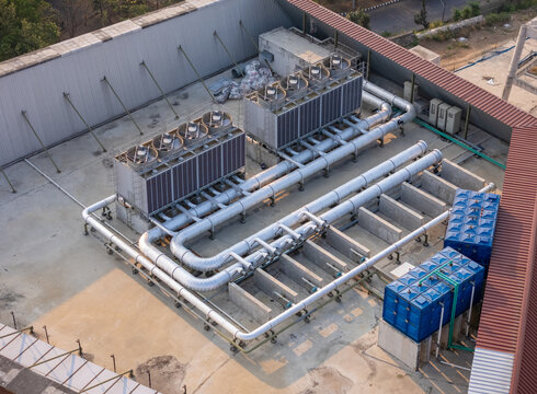 Aerial view of industrial cooling towers and blue water storage tanks installed on a flat rooftop in Surakarta, Central Java, Indonesia.