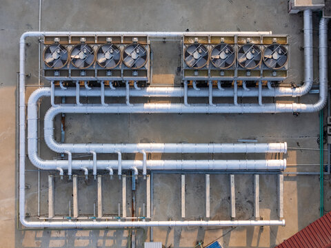 Aerial view of industrial HVAC cooling units with large fans and silver ventilation pipes installed on a flat concrete rooftop in Surakarta, Central Java, Indonesia.