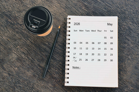 May 2026 desk calendar with disposable coffee cup and pen on wooden table. Directly above. Flat lay.