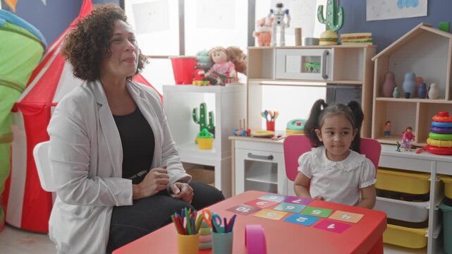 Woman teacher places number card on table and uses hand to point at colored numbers in a child playroom building; concentration learning.