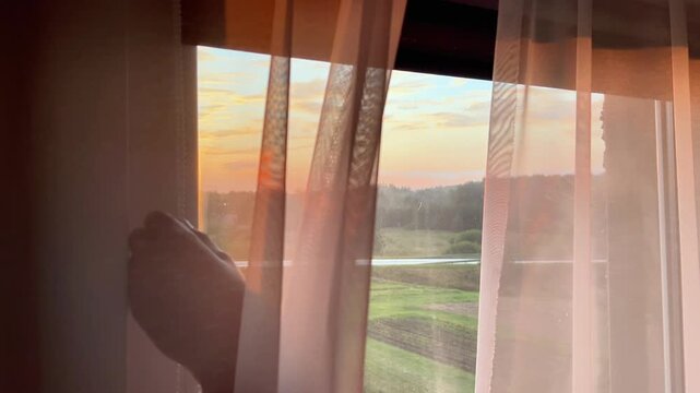 Close up view of hands pulling a roller blind chain to close the window blinds against warm golden sunset light. Evening routine concept.