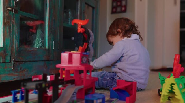 Toddler operates a colorful action playset on the living room floor, exploring movable pieces while developing imagination, coordination and independent problem solving