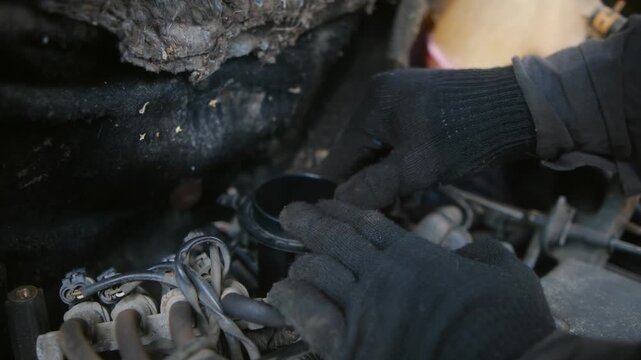 Professional mechanic wearing black gloves carefully repairing a broken and dirty car engine or throttle, performing routine maintenance and diagnostics in an auto repair shop or garage service center
