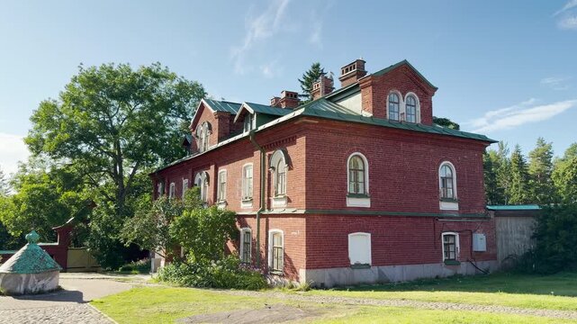 A historic red brick monastery building stands along a sunny pathway on Valaam, Lake Ladoga. This scenic architectural landmark inspires a peaceful, serene, and majestic feeling.