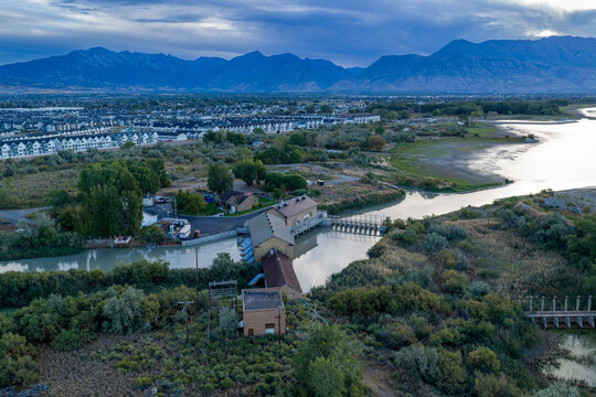 Aerial view of the historical Utah Lake Pumping Plant at the head of the Jordan River, surrounded by vegetation and housing in Saratoga Springs, Utah, United States.