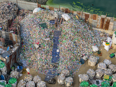 Aerial view of a plastic recycling facility in Bakalia with a worker on a pile of plastic bottles, surrounded by bags of waste and polluted water in Chattogram, Chittagong, Bangladesh.