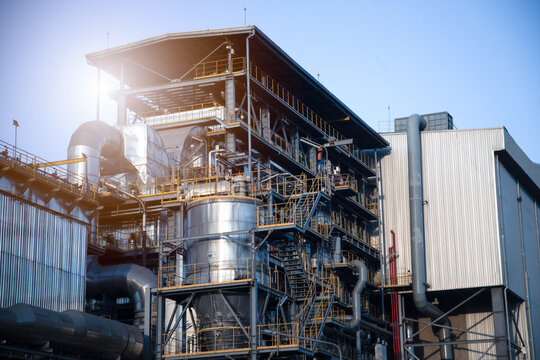 Modern industrial power plant with complex piping and steel structures under a clear sky.Exterior of a large chemical processing factory or biomass energy plant during daytime.