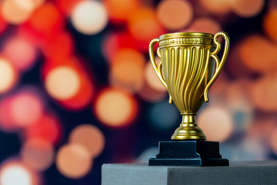 Golden trophy cup against a warm blurred bokeh background with copy space for text. Success, leadership, achievement, victory, award concept.