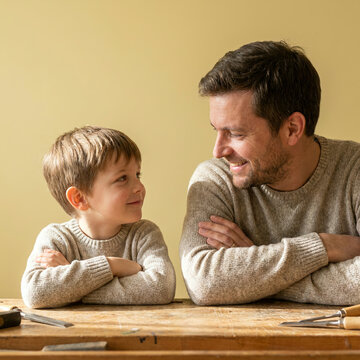 Father and son in matching grey sweaters with arms crossed together indoors