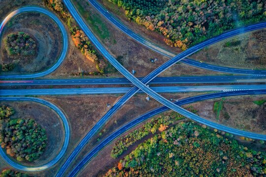 Aerial view of a complex highway interchange with cloverleaf ramps surrounded by dense forest and autumn foliage in Sausheim, Grand Est, France.